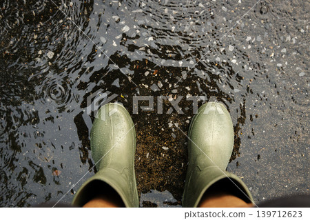 POV shot of person with rain boots standing on wet ground during rainfall, with raindrops in Rainy season POV shot of person with rain boots standing on wet ground during rainfall, with raindrops in Rainy season 139712623