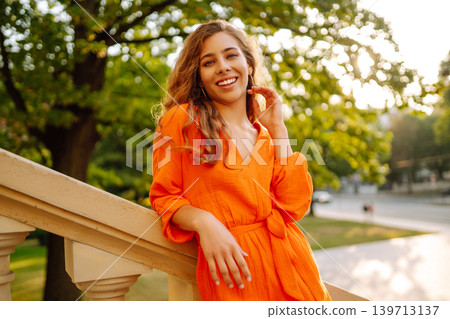 Young woman posing against backdrop of urban landscape in bright orange dress. Concept of lifestyle. 139713137