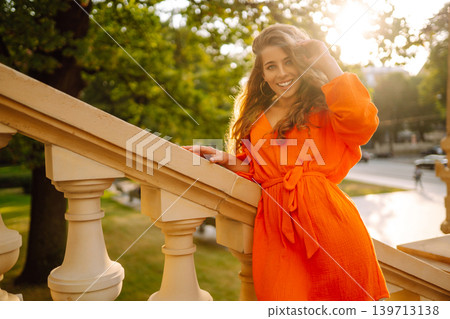 Young woman posing against backdrop of urban landscape in bright orange dress. Concept of lifestyle. 139713138