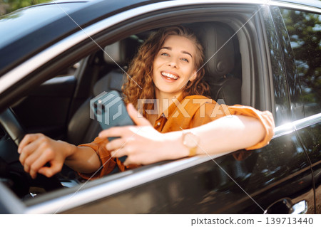 Happy woman in the car in the driver's seat looks at the smartphone. Business, technology concept. Happy woman in the car in the driver's seat looks at the smartphone. Business, technology concept. 139713440