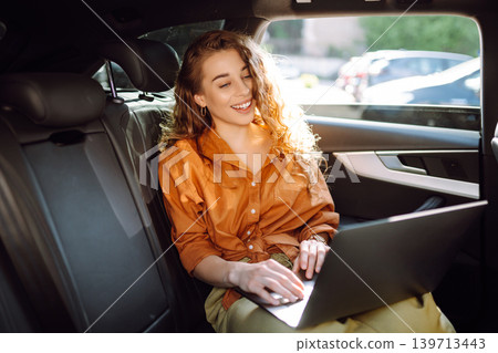 Business beautiful woman with modern laptop sits in back seat of car. Successful startup. Business beautiful woman with modern laptop sits in back seat of car. Successful startup. 139713443