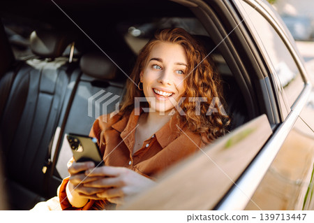 A young woman with a smartphone chats in the back seat of a car. Transport concept. Lifestyle. 139713447