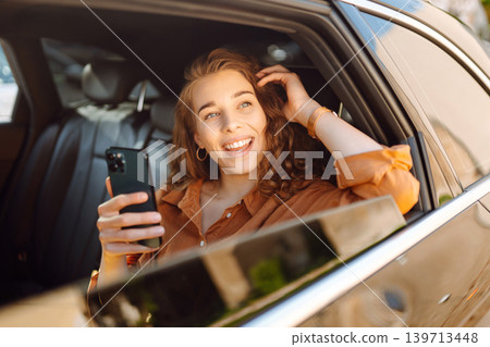 A young woman with a smartphone chats in the back seat of a car. Transport concept. Lifestyle. A young woman with a smartphone chats in the back seat of a car. Transport concept. Lifestyle. 139713448