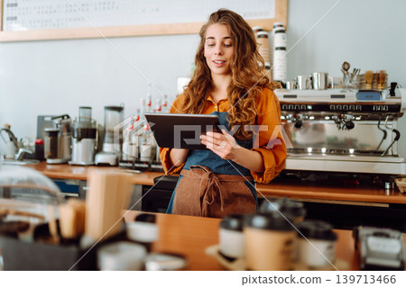 Beautiful woman owner stands behind the counter of a coffee shop. Business concept. Takeaway food. Beautiful woman owner stands behind the counter of a coffee shop. Business concept. Takeaway food. 139713466