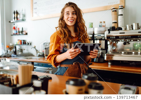 Beautiful woman owner stands behind the counter of a coffee shop. Business concept. Takeaway food. Beautiful woman owner stands behind the counter of a coffee shop. Business concept. Takeaway food. 139713467