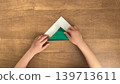 A photo of a child folding green origami paper into a triangle. 139713611