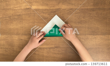A photo of a child folding green origami paper into a triangle. A photo of a child folding green origami paper into a triangle. 139713611