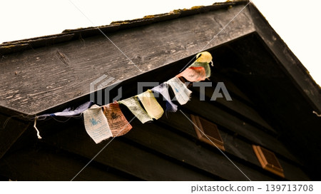 Colorful Buddhist prayer flags under the eave of a wooden building Colorful Buddhist prayer flags under the eave of a wooden building 139713708