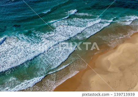 Aerial drone view of waves rolling onto the sandy shoreline at Nobbys Beach in Newcastle, New South Wales, Australia. Aerial drone view of waves rolling onto the sandy shoreline at Nobbys Beach in Newcastle, New South Wales, Australia. 139713939