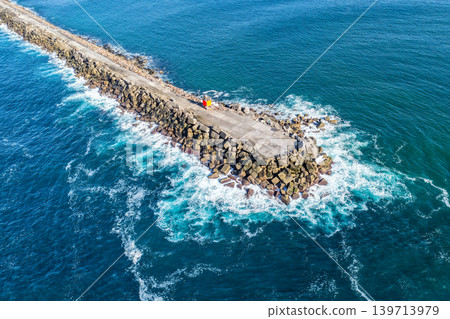 Aerial drone view of the Newcastle breakwall extending into the Pacific Ocean with waves moving along the rocky structure. Aerial drone view of the Newcastle breakwall extending into the Pacific Ocean with waves moving along the rocky structure. 139713979