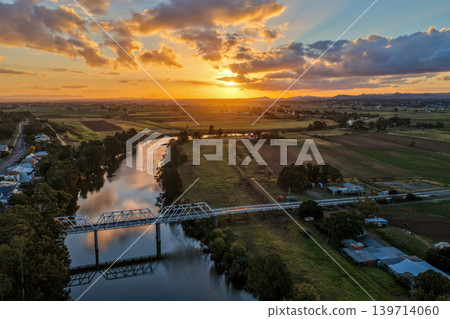 Aerial view of sunset over Morpeth River and bridge in New South Wales, Australia. Scenic landscape showing warm evening light reflecting across water and structure spanning river. 139714060