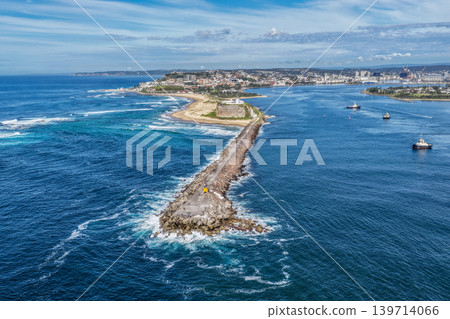 Aerial drone view of Nobbys Breakwall, Nobbys Lighthouse and Nobbys Beach with tug boats operating in Newcastle Harbour. 139714066