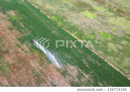 Aerial downward view of travelling irrigator watering farmland in New South Wales, Australia. Agricultural landscape showing irrigation system distributing water across cultivated field from above. Aerial downward view of travelling irrigator watering farmland in New South Wales, Australia. Agricultural landscape showing irrigation system distributing water across cultivated field from above. 139714106
