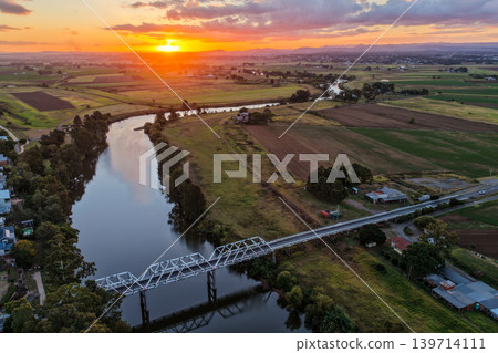 Aerial view of sunset over Morpeth River and bridge in New South Wales, Australia. Scenic landscape showing warm evening light reflecting across water and structure spanning river. Aerial view of sunset over Morpeth River and bridge in New South Wales, Australia. Scenic landscape showing warm evening light reflecting across water and structure spanning river. 139714111