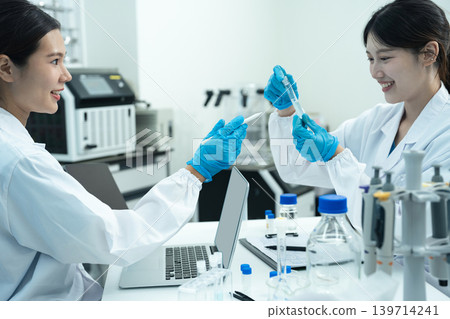 Asian women researchers analyzing cell culture in petri dish near laboratory bottle at workplace. Asian women researchers analyzing cell culture in petri dish near laboratory bottle at workplace. 139714241