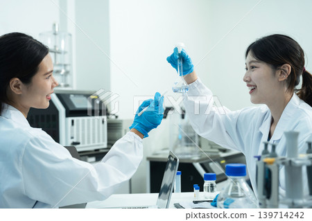 Asian women researchers analyzing cell culture in petri dish near laboratory bottle at workplace. 139714242
