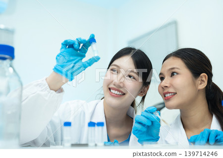 Asian women researchers analyzing cell culture in petri dish near laboratory bottle at workplace. Asian women researchers analyzing cell culture in petri dish near laboratory bottle at workplace. 139714246