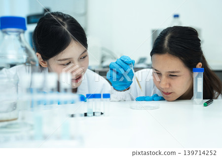 Asian women researchers analyzing cell culture in petri dish near laboratory bottle at workplace. Asian women researchers analyzing cell culture in petri dish near laboratory bottle at workplace. 139714252