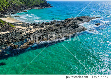 Aerial view of the rocky headland between Seven Mile Beach and Sharkies Beach in Forster NSW Australia. Drone photograph captures rugged coastal formations, turquoise ocean water  139714347