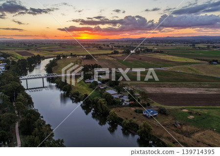 Aerial view of sunset over Morpeth River and bridge in New South Wales, Australia. Scenic landscape showing warm evening light reflecting across water and structure spanning river. Aerial view of sunset over Morpeth River and bridge in New South Wales, Australia. Scenic landscape showing warm evening light reflecting across water and structure spanning river. 139714395
