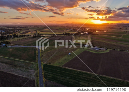Aerial view of sunset over farmland at Morpeth in New South Wales, Australia. Scenic rural landscape showing warm evening light across agricultural fields and countryside. Aerial view of sunset over farmland at Morpeth in New South Wales, Australia. Scenic rural landscape showing warm evening light across agricultural fields and countryside. 139714398