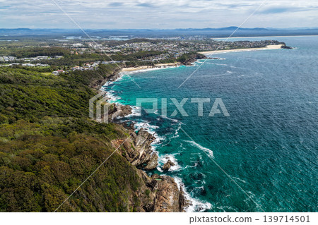 Aerial drone view of a rocky coastline leading towards Burgess Beach and One Mile Beach in Forster. The perspective captures rugged coastal formations, ocean water and natural landscape along the Aerial drone view of a rocky coastline leading towards Burgess Beach and One Mile Beach in Forster. The perspective captures rugged coastal formations, ocean water and natural landscape along the 139714501