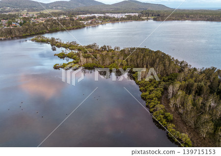Aerial drone view of a small tree covered island surrounded by the calm waters of Wallis Lake in Pipers Bay, Forster, New South Wales, Australia. Aerial drone view of a small tree covered island surrounded by the calm waters of Wallis Lake in Pipers Bay, Forster, New South Wales, Australia. 139715153
