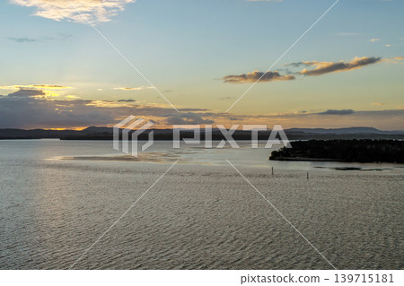 Aerial drone view over Pipers Bay in Forster, New South Wales, Australia with the sun setting behind a cloudy sky. 139715181