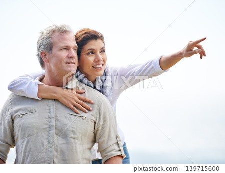Happy, mature couple and pointing on holiday with travel to beach and embrace with love on adventure in summer. Vacation, sightseeing and woman hug man in nature on blue sky with mock up space Happy, mature couple and pointing on holiday with travel to beach and embrace with love on adventure in summer. Vacation, sightseeing and woman hug man in nature on blue sky with mock up space 139715600