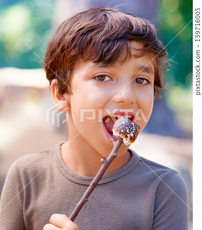 Child, camping and eating a marshmallow in portrait, hungry and fire roast candy in forest. American boy, summer break and smile on face for sugar snack, chocolate and nature on holiday adventure Child, camping and eating a marshmallow in portrait, hungry and fire roast candy in forest. American boy, summer break and smile on face for sugar snack, chocolate and nature on holiday adventure 139716005