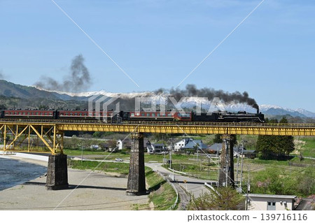 The Ban'etsu Monogatari train crosses the Ichinotogawa Bridge on the Ban'etsu West Line, with the snow-capped Iide Mountain Range in the background. The Ban'etsu Monogatari train crosses the Ichinotogawa Bridge on the Ban'etsu West Line, with the snow-capped Iide Mountain Range in the background. 139716116