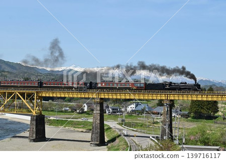 The Ban'etsu Monogatari train crosses the Ichinotogawa Bridge on the Ban'etsu West Line, with the snow-capped Iide Mountain Range in the background. The Ban'etsu Monogatari train crosses the Ichinotogawa Bridge on the Ban'etsu West Line, with the snow-capped Iide Mountain Range in the background. 139716117