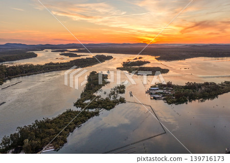 Aerial view of sunset over Wallis Lake in Forster NSW Australia. Drone photograph captures calm waterways, colourful evening sky reflections and the scenic coastal landscape Aerial view of sunset over Wallis Lake in Forster NSW Australia. Drone photograph captures calm waterways, colourful evening sky reflections and the scenic coastal landscape 139716173