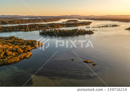 Aerial view of sunset over Wallis Lake in Forster NSW Australia. Drone photograph captures calm waterways, colourful evening sky reflections and the scenic coastal landscape Aerial view of sunset over Wallis Lake in Forster NSW Australia. Drone photograph captures calm waterways, colourful evening sky reflections and the scenic coastal landscape 139716219