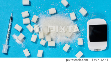 A glucometer, insulin syringe, and sugar cubes on a blue background, a concept for blood sugar control and diabetes treatment. A glucometer, insulin syringe, and sugar cubes on a blue background, a concept for blood sugar control and diabetes treatment. 139716431