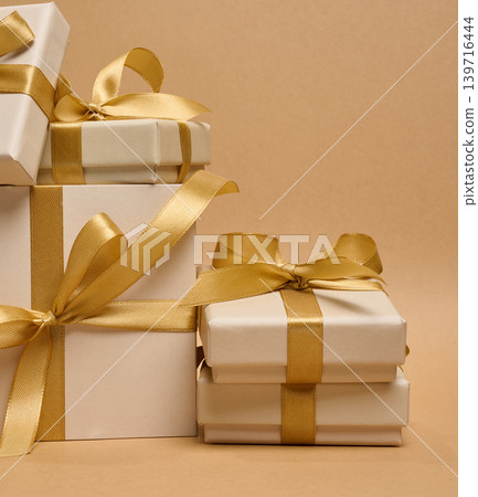 A stack of cream-colored gift boxes tied with gold satin ribbons and bows A stack of cream-colored gift boxes tied with gold satin ribbons and bows 139716444