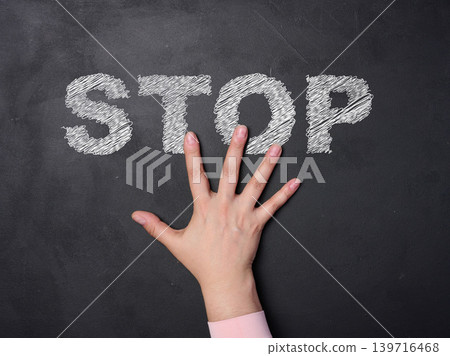 A person's hand covers the word STOP written in chalk on a blackboard, expressing protest, a strong cessation of an action A person's hand covers the word STOP written in chalk on a blackboard, expressing protest, a strong cessation of an action 139716468