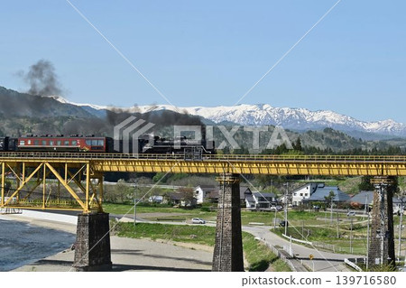 The Ban'etsu Monogatari train crosses the Ichinotogawa Bridge on the Ban'etsu West Line, with the snow-capped Iide Mountain Range in the background. The Ban'etsu Monogatari train crosses the Ichinotogawa Bridge on the Ban'etsu West Line, with the snow-capped Iide Mountain Range in the background. 139716580