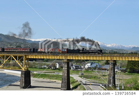 The Ban'etsu Monogatari train crosses the Ichinotogawa Bridge on the Ban'etsu West Line, with the snow-capped Iide Mountain Range in the background. The Ban'etsu Monogatari train crosses the Ichinotogawa Bridge on the Ban'etsu West Line, with the snow-capped Iide Mountain Range in the background. 139716584
