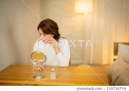 A woman who worries about the condition of her skin in her bedroom at night. A woman who worries about the condition of her skin in her bedroom at night. 139716759