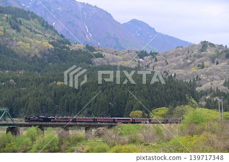 The SL Ban'etsu Monogatari train crosses the Agano River with snow-capped mountains in the background on the Ban'etsu West Line. The SL Ban'etsu Monogatari train crosses the Agano River with snow-capped mountains in the background on the Ban'etsu West Line. 139717348