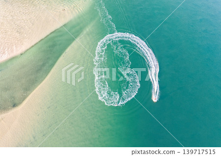 Aerial view of a jet ski creating wake patterns in the turquoise waters of Wallis Lake in Forster NSW Australia. Drone photograph captures the personal watercraft moving across clear blue water 139717515