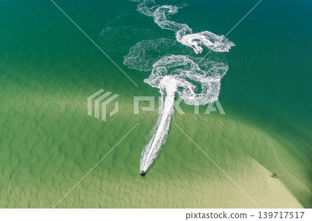 Aerial view of a jet ski creating wake patterns in the turquoise waters of Wallis Lake in Forster NSW Australia. Drone photograph captures the personal watercraft moving across clear blue water Aerial view of a jet ski creating wake patterns in the turquoise waters of Wallis Lake in Forster NSW Australia. Drone photograph captures the personal watercraft moving across clear blue water 139717517
