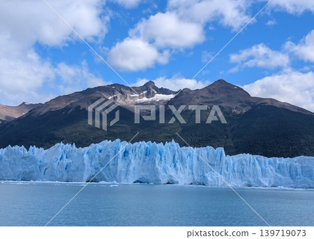 Blue ice wall of Perito Moreno Glacier against dark mountain peaks and blue sky Blue ice wall of Perito Moreno Glacier against dark mountain peaks and blue sky 139719073