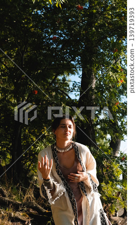 A beautiful brunette dressed in boho style meditates and dances in the forest. A magical ritual takes place against a green forest backdrop. A beautiful brunette dressed in boho style meditates and dances in the forest. A magical ritual takes place against a green forest backdrop. 139719393