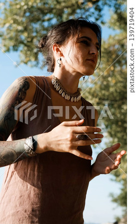 A beautiful brunette dressed in boho style meditates and dances in the forest. A magical ritual takes place against a green forest backdrop. A beautiful brunette dressed in boho style meditates and dances in the forest. A magical ritual takes place against a green forest backdrop. 139719404