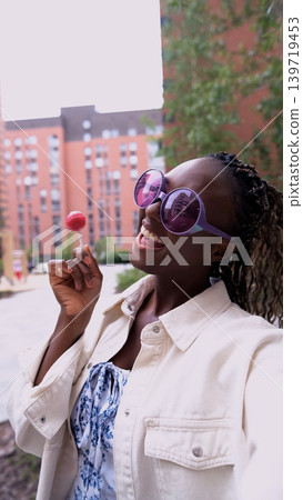 A beautiful woman poses for a smartphone selfie, holding a sweet lollipop. A beautiful woman poses for a smartphone selfie, holding a sweet lollipop. 139719453