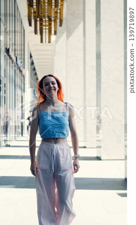 A portrait of a teenage girl with red hair posing for a photo near columns at the entrance to a business center 139719897