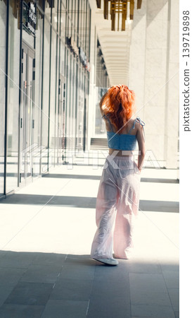 A portrait of a teenage girl with red hair posing for a photo near columns at the entrance to a business center 139719898