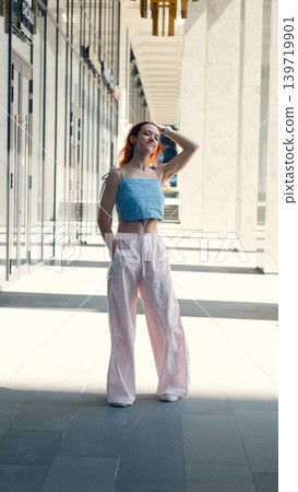 A portrait of a teenage girl with red hair posing for a photo near columns at the entrance to a business center A portrait of a teenage girl with red hair posing for a photo near columns at the entrance to a business center 139719901